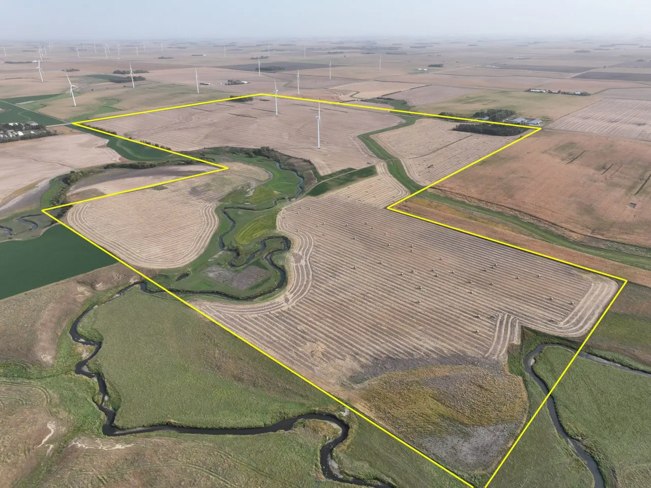 Aerial view of expansive farmland outlined in yellow, featuring wind turbines, harvested fields, and winding streams, conveying a serene, agricultural landscape.