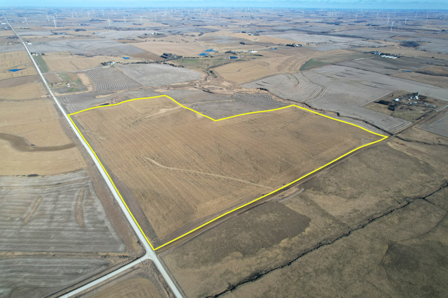 Aerial view of expansive farmland outlined in yellow, surrounded by brown fields with a distant horizon. Calm, rural landscape under a clear sky.