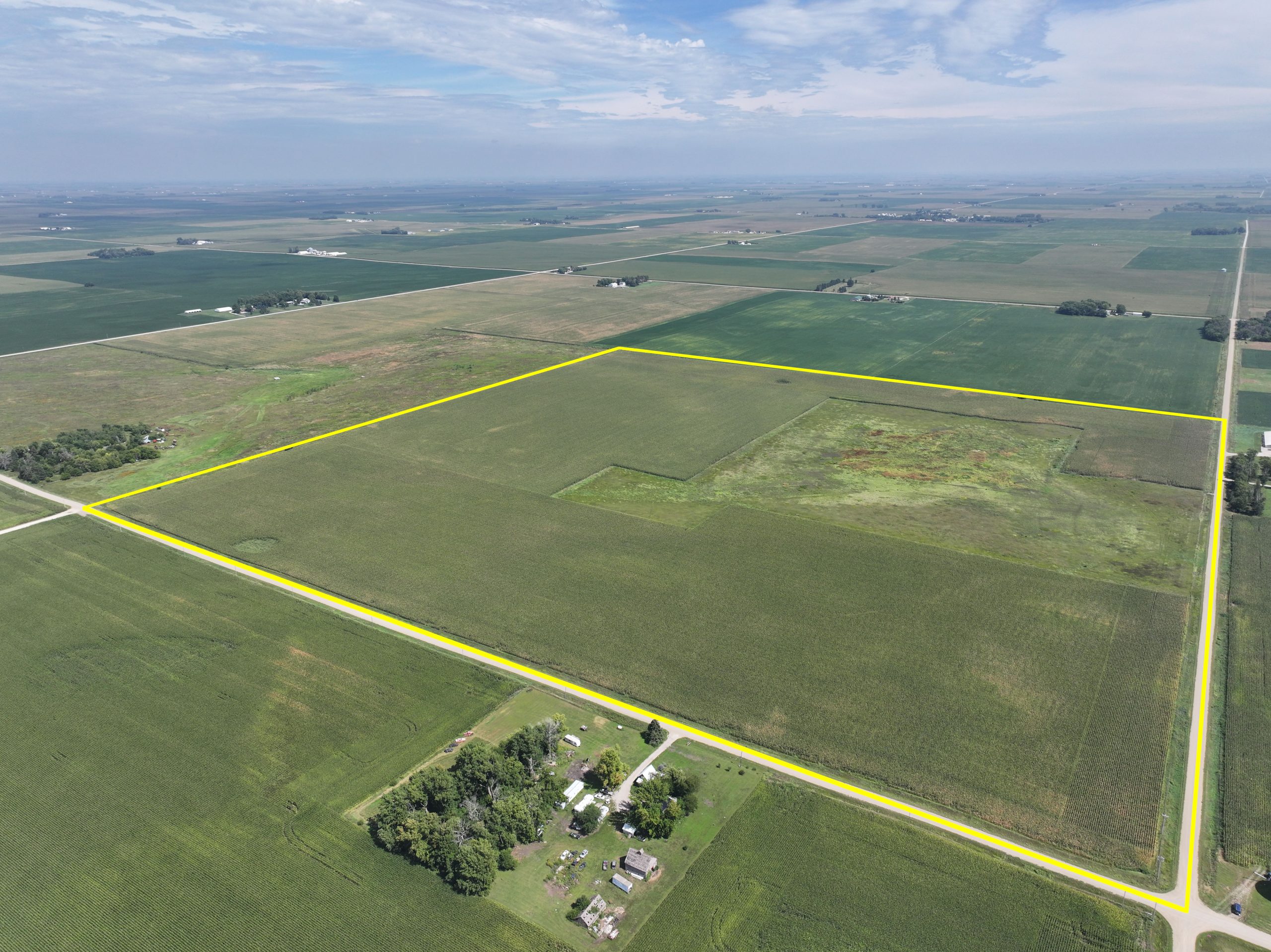 Aerial view of a farmland tract outlined in yellow, with a small farmstead nearby.
