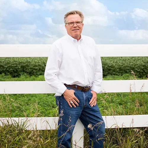 jon-hjelm-auctioneer Jon Hjelm, founder and auctioneer at The Acre Company, standing by a fence post on some farmland